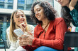 © Connect Images - Three smiling women sharing a moment while looking at a smartphone together, Berlin, Germany