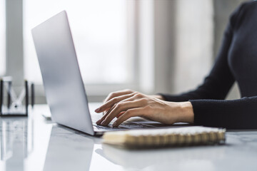 Wall Mural - Set against a blurred office scene, the image reveals a close-up of a woman's hands typing on a modern laptop keyboard