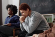 © Seventyfour - Side view portrait of teenage boy struggling with mental health issues sitting on chair during support group meeting copy space