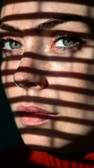 Wall Mural - A close-up portrait of a woman with striking green eyes, illuminated by light creating dramatic shadows across her face.