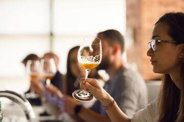 Woman Looking and Analyzing Color of Beer. Group of Participants Tasting Beer on Beer Craft Lecture. Female sommelier tasting beer during training beer school. 