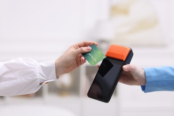 Wall Mural - Woman paying with credit card via terminal against blurred background, closeup