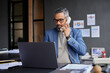 © Rido - Mature indian businessman on call while working on laptop
