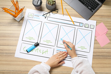 Wall Mural - website designer creating wireframe on paper with pen at wooden table, top view