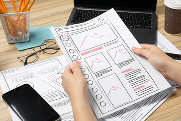 Wall Mural - website designer holding wireframe at wooden table with smartphone and laptop, closeup