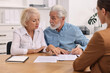 © New Africa - Pension plan. Senior couple consulting with insurance agent at wooden table indoors