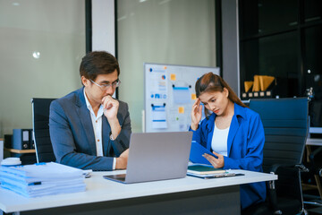 Wall Mural - A stressed businessman and woman sit at a desk, overwhelmed by business challenges. They discuss problems,financial pressures, and strategy, seeking solutions to manage work, deadlines, and economic