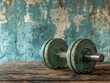 © BerkahStock - Rustic green dumbbell on weathered wooden table against a grunge teal wall.