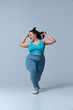 © Lustre Art Group  - Chubby woman in blue top and leggings stepping forward with hair flowing, smiling while performing lively motion, against white studio background. Concept of beauty, fitness, movement, dance and music