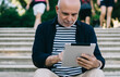 © BullRun - Focused aged man using tablet on steps in park