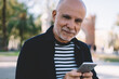 © BullRun - Happy aged man using smartphone in modern park