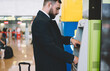 © BullRun - Side view of Caucasian businessman dressed in formal clothing using ATM machine for getting international cash after departure to airport, corporate director enter pin code protection of debit card