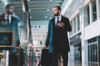 © BullRun - Contemplative corporate director with suitcase baggage and smartphone technology thoughtful looking away while searching terminal gate in airport, Caucasian employer 30s during business trip