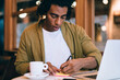 © BullRun - Thoughtful ethnic man taking notes in cafe