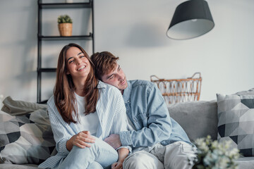 Wall Mural - Portrait of young 20s just married couple in love posing photo shooting seated on couch in modern studio apartments, concept of capture happy moment, harmonic relationships, care and sincere feelings.