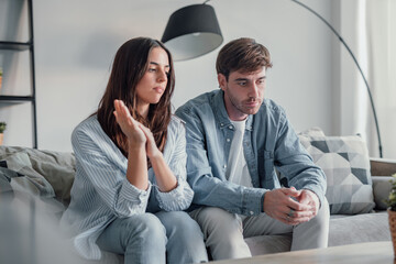 Beautiful lady is depressed, sitting on the couch talking to man, having a dispute with husband or girlfriend, looking desperate and hopeless, having unresolved problem or question.