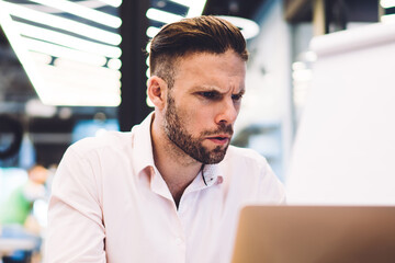 Puzzled male entrepreneur watching video webinar feeling puzzled on received financial information, Caucasian businessman using office internet connection for working with web documents on laptop