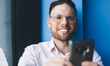 © BullRun - Half length portrait of cheerful male blogger in eyewear smiling at camera while creating web publication on cellphone, happy man in spectacles enjoying leisure time for web mobile communication