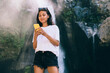 © BullRun - Cheerful female tourist using phone near waterfall