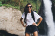 © BullRun - Happy female tourist with backpack standing near waterfall
