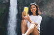 © BullRun - Cheerful female traveler making selfie near waterfall