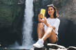 © BullRun - Cheerful female traveler making selfie near waterfall