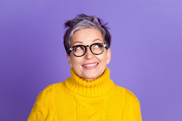 cheerful mature woman in yellow sweater with glasses looking up against purple background