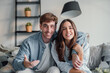 © Daniel - Head shot positive loving bonding married couple sitting on comfortable sofa, looking at camera, holding video call with friends. Happy family bloggers recording video for personal channel at home..