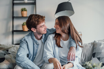 Wall Mural - Portrait of young 20s just married couple in love posing photo shooting seated on couch in modern studio apartments, concept of capture happy moment, harmonic relationships, care and sincere feelings.