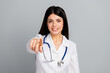 © deagreez - Professional female doctor pointing forward with a confident smile on a gray background