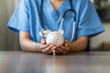 © Dee karen - Nurse or doctor with stethoscope holding piggy bank in hand. Concept of medical expenses, finance, saving money, health insurance, medicine, donation and pension. Healthcare service cost.