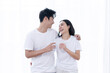 © charnsitr - Asian couple enjoying drinking water and sharing smiles against white curtain background