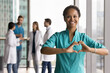 © fizkes - Portrait of young African woman cardiologist wear turquoise scrub standing in clinic office, make heart shape with hands, symbol of care, medical insurance, heart disease prevention check-up services