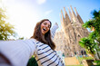© CarlosBarquero - Young funny caucasian women taking a selfie in front of Sagrada Familia in Barcelona. Smiling beautiful girl on street of European city enjoying vacation happy and smiling. Funny tourism people