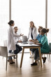 © fizkes - Vertical shot young healthcare medical workers discussing patient case in meeting room, listen speech, opinion, share experience Indian female in white lab coat. Collaboration between hospital staff