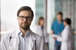 © fizkes - Young Caucasian doctor, therapist or cardiologist posing in clinic office, wearing glasses and white coat, looking at camera with serious and focused expression. Healthcare worker head shot portrait