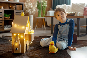 Child, cute boy, playing with toys in a playroom, teddy bear and little ducks with a paper house