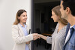 © fizkes - Positive confident realtor shaking hands with couple of young renters at entrance of rental apartment, smiling, finishing meeting. Happy customers giving handshake to agent, finding flat for rent