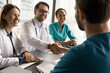 © fizkes - Diverse professionals, medical workers finish concilium, shaking hands at conference table, gathered in modern clinic boardroom express mutual respect, make agreement, sign of collaboration and trust