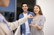 © fizkes - Happy couple buying new house, getting key from realtor, meeting with seller, real estate agent outdoors at apartment entrance. Positive young man and woman renting flat
