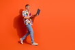 © deagreez - A confident young man in a vibrant, stylish shirt walks against an orange background while looking at his laptop.