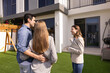 © fizkes - Happy real estate agent woman showing house for sale to young couple of customers, buyers, standing on yard, pointing at exterior, speaking, smiling. Renters meeting with realtor for viewing