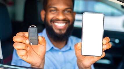 Wall Mural - Car Renting App. Happy Black Man Showing Key And Smartphone With Blank White Screen Through Window While Sitting In His Automobile In Dealership Center Or Rental Office, Closeup Shot, Mockup