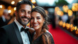 © Kevin - A couple dressed in formal evening wear, smiling as they pose on a red carpet at an elegant black tie event