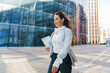 © muse studio - Businesswoman walking confidently with a tablet in a modern urban setting during daytime