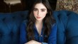 © JO BLA CO - A young woman is seated on a blue velvet couch, wearing a denim shirt. Soft light highlights her features, creating an inviting and elegant atmosphere in the room