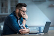 © Prostock-studio - Attractive tired bored programmer digital specialist manager work remotely online overtime. Concentrated sad pensive young bearded guy looks at laptop and presses hand to mouth in kitchen interior