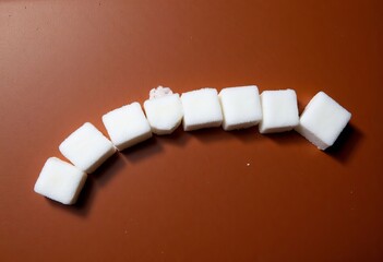 Wall Mural - Nine sugar cubes on brown surface with small pink crumbs on one