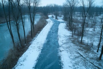 Aufkleber - A snow-laden road meanders through a dense, serene winter forest, with snow-covered trees creating a peaceful atmosphere and soft light illuminating the path