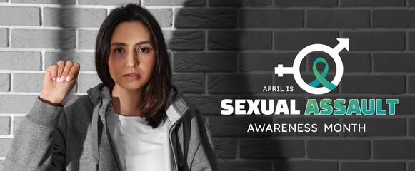 Wall Mural - Bruised young woman with clenched fist near grey brick wall. Banner for Sexual Assault Awareness Month